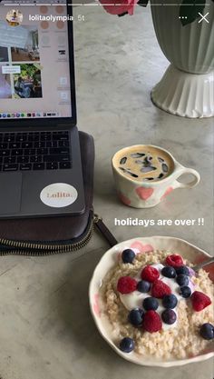 a bowl of oatmeal with berries and blueberries in front of a laptop