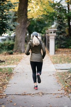 a woman running down a sidewalk with trees in the background and leaves on the ground