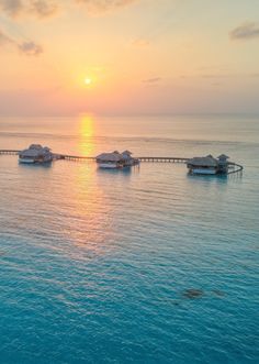 the sun is setting over some water with huts on stilts in the middle of it