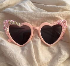 ITEM DETAILS *Heart shaped custom sunglasses in pink or white *Each pair is handcrafted and can accommodate any special requests or names you would like reflected. *Standard design will be Cherry and rhinestone decoration or rhinestone heart decoration. *Pink glasses in picture are reflecting the Cherry decoration +White glasses in picture are reflecting the Heart rhinestone decoration. Customizable Pink Sunglasses For The Beach, Personalized Pink Sunglasses For Beach, Playful Personalized Pink Sunglasses, Custom Name Pink Sunglasses With Adjustable Fit, Pink Sunglasses With Custom Name And Adjustable Fit, Pink Plastic Sunglasses For Birthday, Personalized Pink Sunglasses As A Gift, Pink Personalized Sunglasses For Gift, Fun Pink Sunglasses For Gift