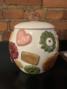 a ceramic jar with hearts and other things on it sitting on a table next to a brick wall