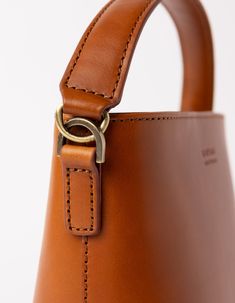 This classy bucket bag has a roomy interior and a slip-in pocket to grab your small essentials in a sec. Designed with a flat bottom, Bobbi stands on her own, making a true statement. Carry her with the top handle or wear her as a cross body bag. Want to spice things up? Her dog hook clasp allows you to mix and match our Webbing straps! Bobbi enjoys a night out or a trip to the beach. She's our go-to girl for every occasion. Check out Bobbi Bucket Bag Maxi, her newer bigger sister! OMB-E139BV Luxury Brown Smooth Grain Bucket Bag, Formal Rectangular Bucket Bag With Leather Handles, Classic Bucket Bag With Leather Handles, Cognac Bucket Bag With Removable Pouch For Everyday Use, Classic Brown Bucket Bag With Top Handle, Classic Bucket Bag With Detachable Handle For Daily Use, Modern Cognac Bucket Bag With Double Handle, Cognac Leather Bucket Bag With Detachable Handle, Brown Bucket Bag With Leather Lining