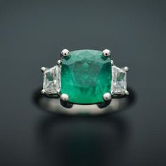 This Elegant Platinum three stone ring has a Natural Cushion Cut Colombian Emerald from the Top Muzo Mine with a GIA Certificate. The side stones are Natural Brilliant Cut Trapezoid Pair of Matching Diamonds. GIA#5202111099 3.34 Carat Cushion Modified 9.64x8.93x5.64 with moderate F2 clarity enchancement. 2 Matching Trapezoid Brilliant Cut Diamonds weigh 0.71 carats total weight and are graded G in color and SI1 to SI2 in clarity. Platinum weight is 5.14 DWT. Ring can be sized. Three Stone Diamond Gemstones For Anniversary, Luxury Three Stone Gemstones For Anniversary, Luxury Three Stone Emerald Ring, Luxury Emerald Three Stone Ring For Formal Occasions, Luxury Three Stone Emerald Ring For Formal Events, Luxury Three Stone Emerald Ring For Formal Occasions, Luxury Three-stone Emerald Ring, Formal Three Stone Emerald Ring In Fine Jewelry Style, Three Stone Diamond Gemstones For Wedding