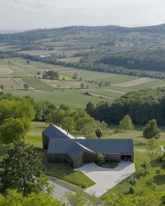 an aerial view of a house in the middle of a green field with trees and rolling hills