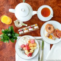 a table topped with plates of food next to cups of tea and orange juice on top of a wooden table