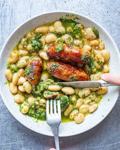 someone is holding a fork over a bowl of beans and broccoli with chicken