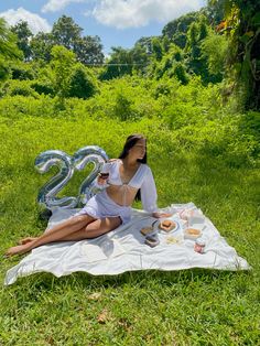 a woman sitting on top of a blanket in the middle of a field eating food