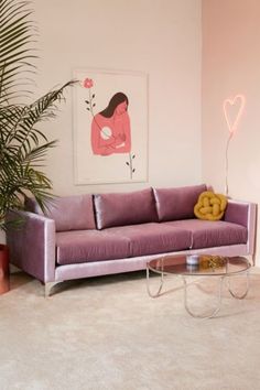 a pink couch sitting in the middle of a living room next to a potted plant