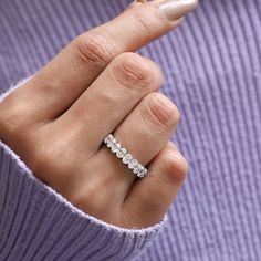 a woman's hand with a diamond ring on her left finger, in front of a purple sweater