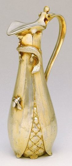 a gold colored pitcher with a fish on it's body and a flower in its mouth