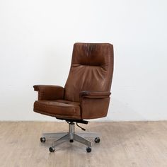 a brown leather office chair sitting on top of a hard wood floor next to a white wall