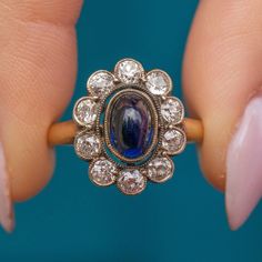 a woman's hand holding a ring with an oval shaped blue stone surrounded by small white diamonds