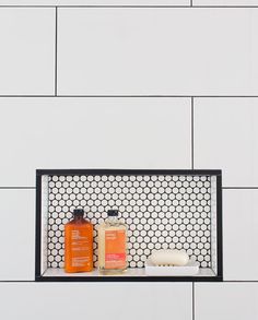 a shelf with two bottles and soaps on it in front of a white tiled wall