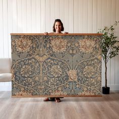 a woman holding up a large tapestry in front of her face