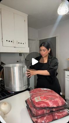 a woman standing in a kitchen next to a pot with meat on top of it