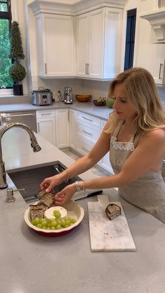 a woman cutting up food on top of a kitchen counter next to a bowl of grapes