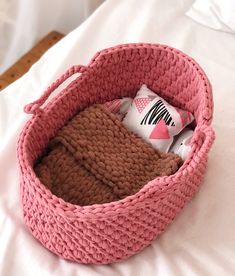 a crocheted pink basket is sitting on a white bed with pillows and blankets