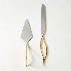 two silver and gold utensils on a white surface with one being cut in half