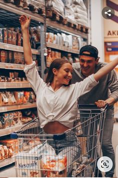 a man and woman pushing a shopping cart through a grocery store aisle with their arms in the air