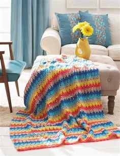 a crocheted blanket on a couch with yellow flowers in a vase next to it