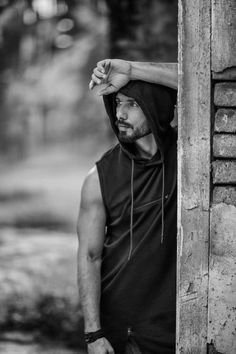 black and white photograph of a man leaning against a wooden wall wearing a hoodie