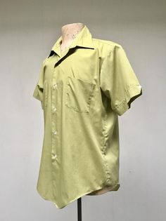 * Men's casual shirt c 1970s* Green polyester-cotton blend fabric * Medium pointed collar* Double chest patch pockets * Short, set-in sleeves with sewn down notched cuff with button detail* Action pleats below back yoke* 6 button front closure* Long tailsLabel: Master Built - Permanent Press - 15 1/2Excellent conditionChest: 44Shoulder: 18Sleeve: 9Length: 31 (center back)Garments are flat-measured. Please compare these measurements to another flat-measured garment that fits you correctly for siz Classic Green Collared Short Sleeve Shirt, Retro Green Collared Shirt, Spring Retro Cotton Camp Shirt, Retro Cotton Camp Shirt For Spring, Cotton Short Sleeve Shirt With Johnny Collar And Pockets, Green Retro Cotton Shirt, Retro Cotton Collared Camp Shirt, Green Retro Relaxed Fit Camp Shirt, Retro Green Relaxed Fit Camp Shirt