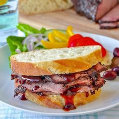 a roast beef sandwich with cranberry sauce on a white plate next to fresh vegetables