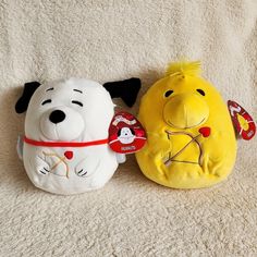 two stuffed animals sitting on top of a white carpet next to each other and one has a red ribbon around it's neck