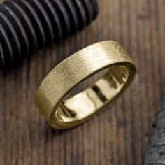 a gold wedding ring sitting on top of a wooden table next to a black object