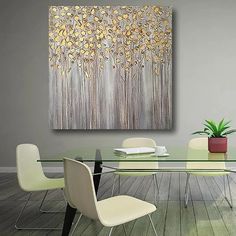 a glass dining table with white chairs and a painting on the wall above it that has gold leaves