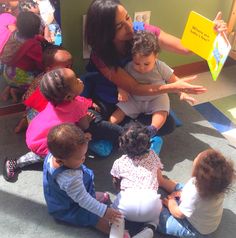 a group of children sitting on the floor in front of a woman holding a book