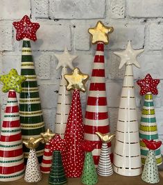 christmas trees are lined up against a brick wall with gold stars on the top and bottom