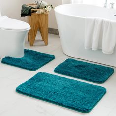 two bath mats on the floor in front of a toilet and tub with blue rugs