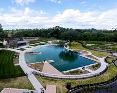 an aerial view of a large swimming pool surrounded by green grass, trees and buildings