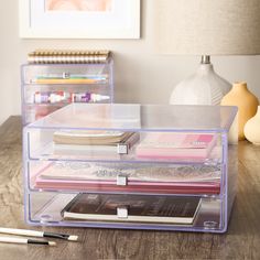 two clear drawers with books and magazines in them on a table next to a lamp