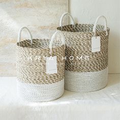 two woven baskets with tags on them sitting next to each other in front of a wall