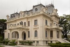 a large white building with many windows and balconies on the top floor, surrounded by greenery