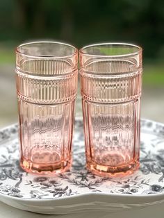 two pink glasses sitting on top of a white and black plate next to each other