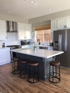 a kitchen with an island and three stools in it, along with stainless steel appliances