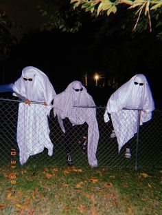 two white ghost costumes hanging on a fence in front of some trees and grass at night