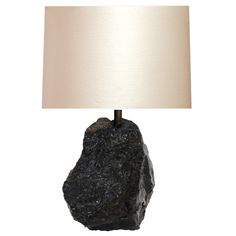 a black rock lamp with a white shade on the base and a beige linen light