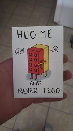 a hand holding a card with a cartoon character on it that says hug me and never lego