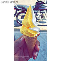 a hand holding an ice cream cone with yellow frosting on it and motorcycles in the background