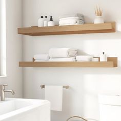 two wooden shelves above a white bathtub in a bathroom with towels and toilet paper