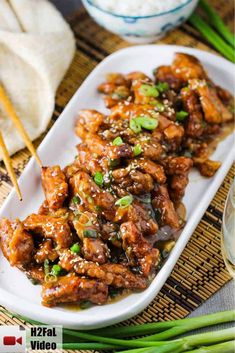 chicken with sesame seeds and green onions served on a white platter next to chopsticks