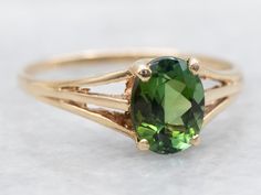 Elevate your style with this gorgeous ring! The stunning oval cut green tourmaline shines brilliantly, while the triple shank design adds a unique touch of elegance. The perfect solitaire ring for the discerning customer! Metal: 14K Yellow Gold Gem: Green Tourmaline 1.29 Carats Gem Measurements: 6.0 x 7.8 mm, Oval Ring Size: 8.50 Marks: "14KFF" Stamped on the inside band SKU #: A44126 Each piece has been identified and graded by a Graduate Gemologist who has been certified by the Gemological Institute of America (GIA). We have six brick-and-mortar storefronts in Maine, Massachusetts, and New Hampshire and have been in business for over 25 years! Please visit our Shop's About Page or our website for more information about our jewelry. For questions about diamond grading, we recommend the  G Split Shank Ring, Gorgeous Ring, Oval Ring, Oval Rings, Tourmaline Ring, Split Shank, Green Tourmaline, New Hampshire, Solitaire Ring