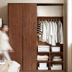 a person walking past a wooden closet with clothes hanging on it