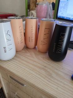 four different colored tumblers sitting on top of a wooden table next to a computer