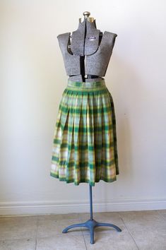 Just an absolutely gorgeous, classic 1950s circle skirt made of a substantial, quality wool fabric in shades of green, yellow, beige and tan. This is a full 360-degree circle skirt, gathered with wide pleats into the waistband. Closes with two grey moonglow buttons and a small metal Lightning zipper. Falls to about mid-calf. No label, perhaps homemade. Condition: very good. It has one small hole on the back which I darned, see last photo. I am not the world's best seamstress, so you may prefer t Retro Green A-line Skirt, Vintage Full Skirt With Accordion Pleats, Fitted Green Accordion Pleated Skirt, Green Accordion Pleats Skirt, Vintage Pleated Plaid Skirt, Vintage Plaid Full Skirt, Vintage Fitted Green Skirt, Retro Green Pleated Skirt, Serious Cat