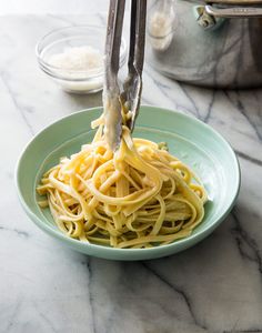 someone is using tongs to eat spaghetti on a green plate with white sauce and grated parmesan cheese